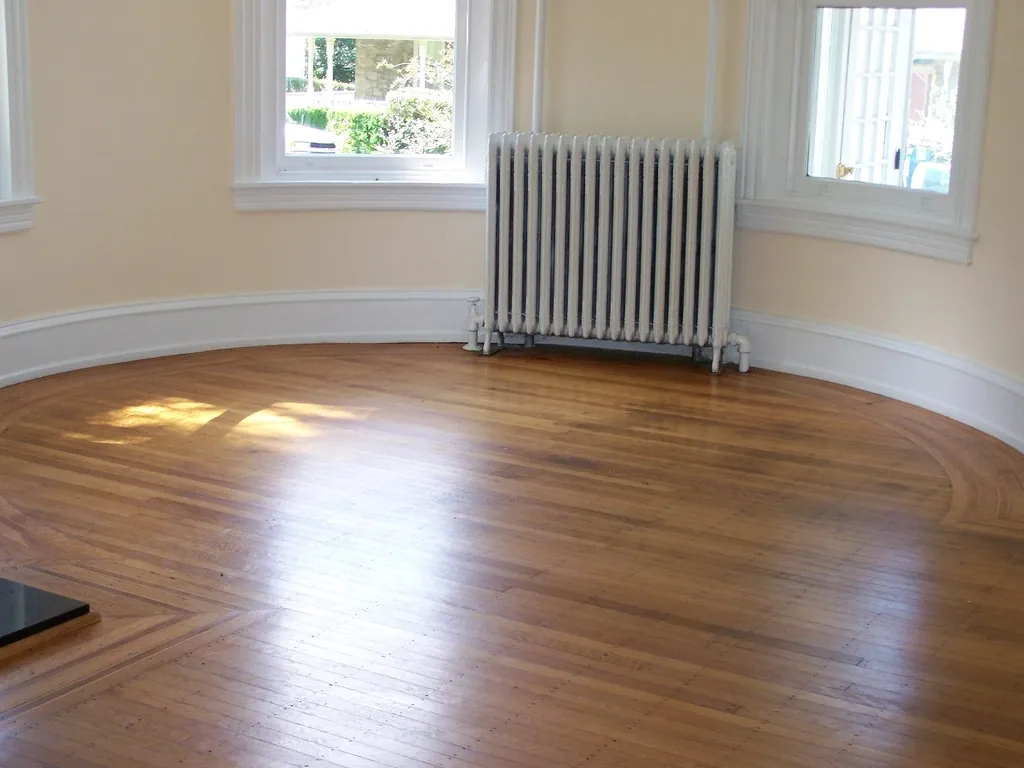 Empty room with wood floors, tall windows and a radiator