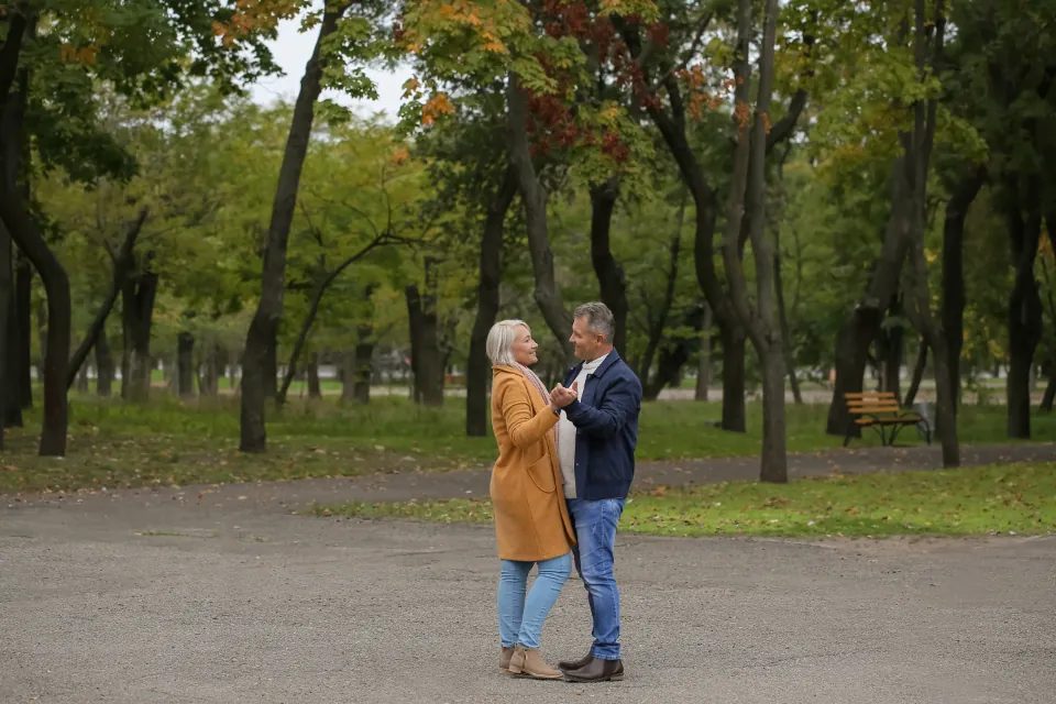 Older couple dancing together on a path in an autumn park