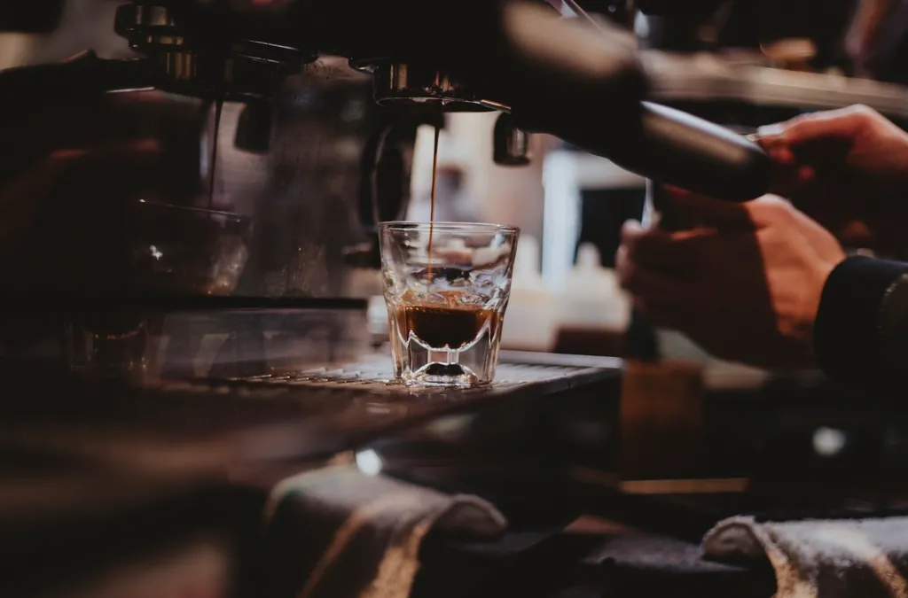 Espresso pouring into a small glass at a coffee bar
