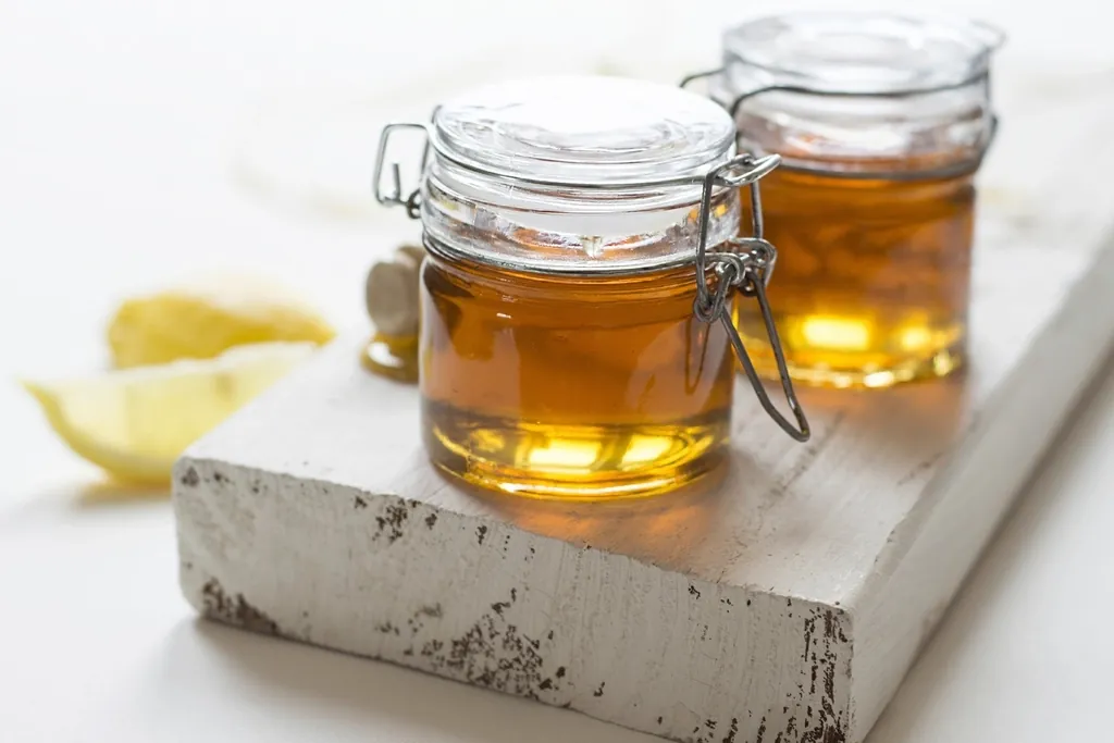 Two glass jars of golden syrup beside lemon wedges