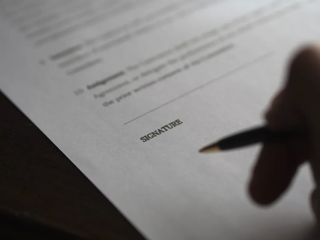 Hand holding a pen over the signature line of a printed agreement