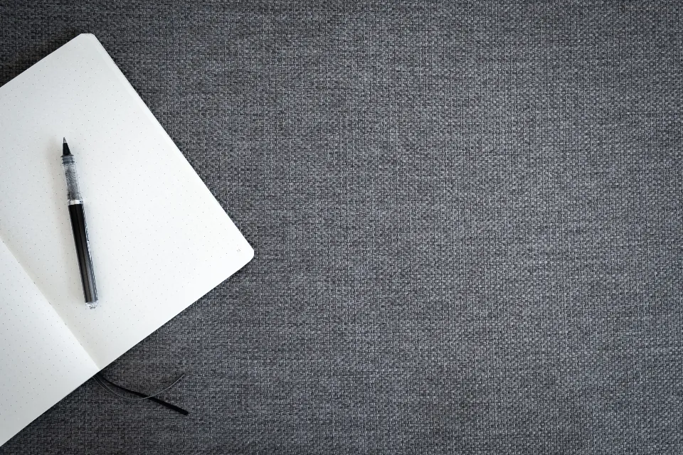 Open blank notebook with a black pen on a gray fabric surface