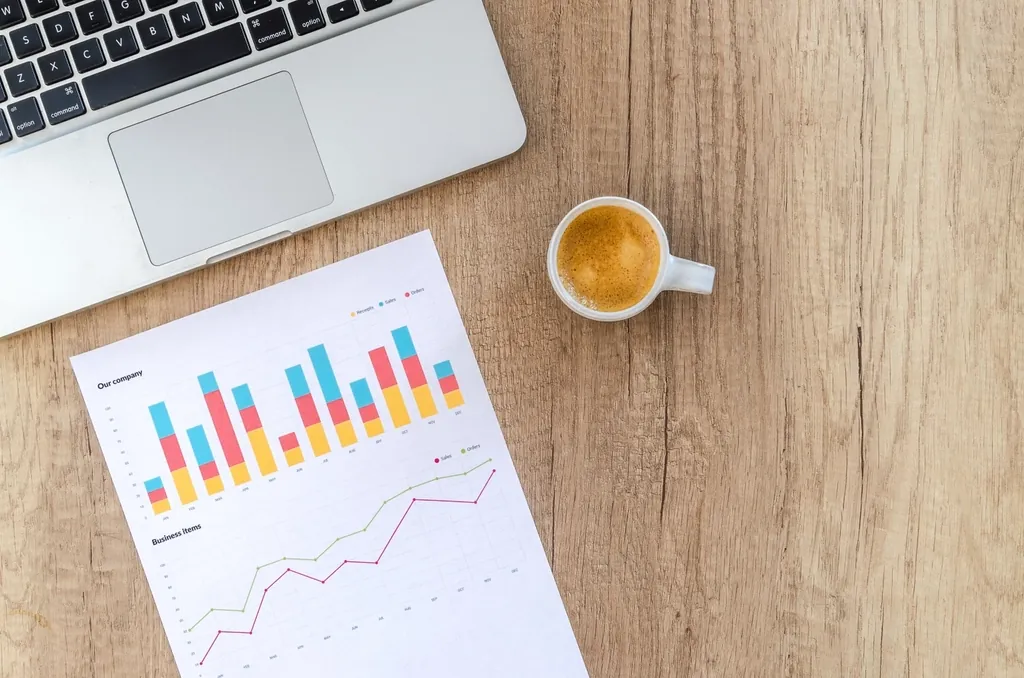 Printed bar and line charts beside a laptop and an espresso cup
