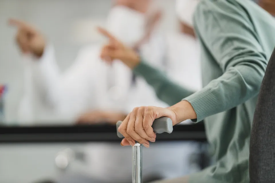 Older adult's hand on a walker with a caregiver nearby