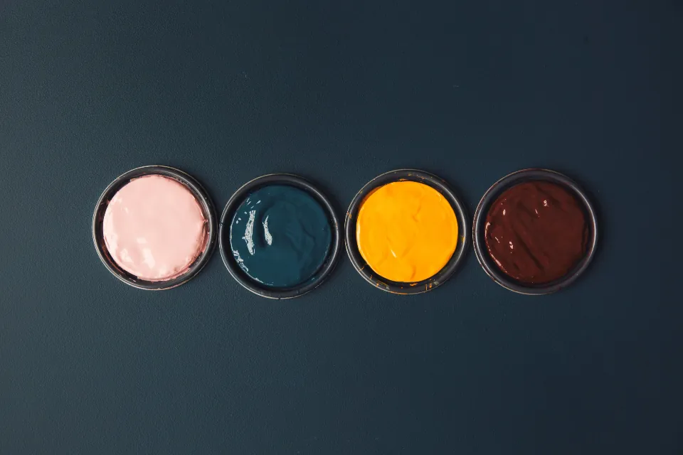 Four open cans of paint in pink, teal, yellow and brown seen from above