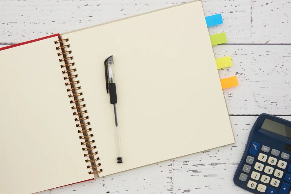 Open spiral notebook with a pen beside a calculator on a white table
