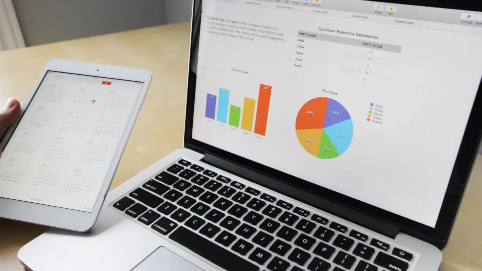 Laptop with bar and pie charts beside a tablet calendar, the kind of report a fractional CFO in NJ reviews