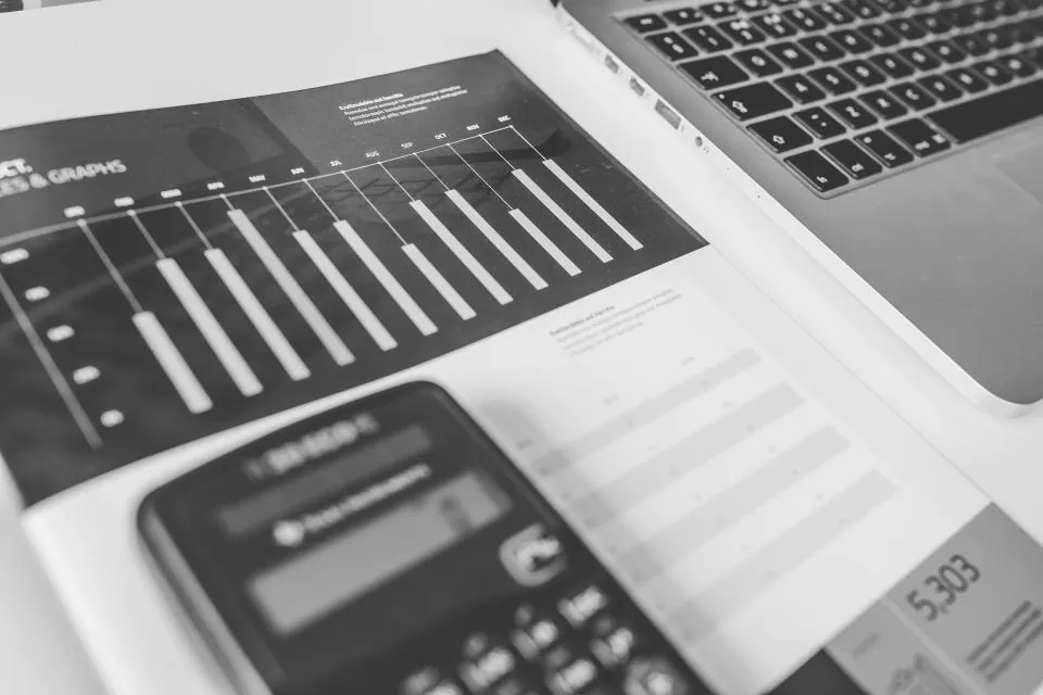 Printed bar charts beside a calculator and laptop keyboard, in black and white