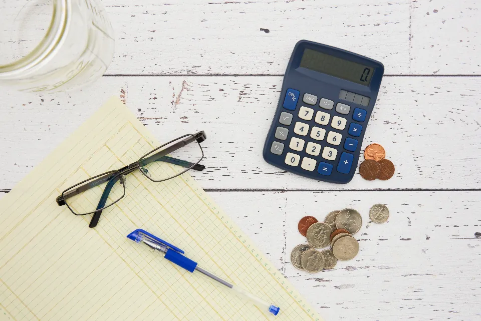 Calculator, coins, eyeglasses and a pen on a ledger sheet