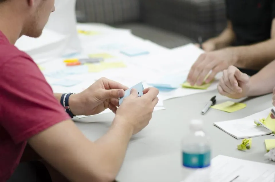 Coworkers' hands sorting sticky notes on a table during a planning session