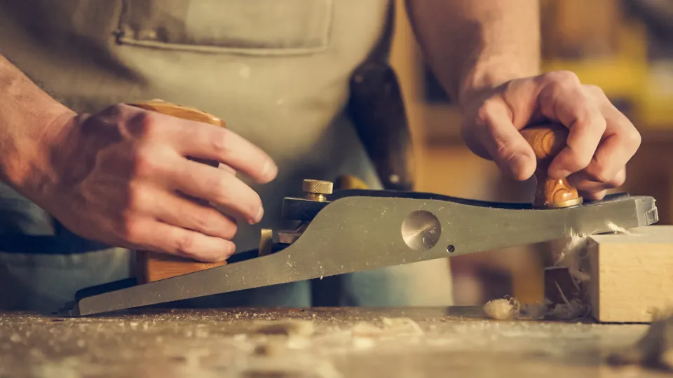 Carpenter's hands guiding a hand plane along a board, a skill to vet when hiring a contractor in NJ