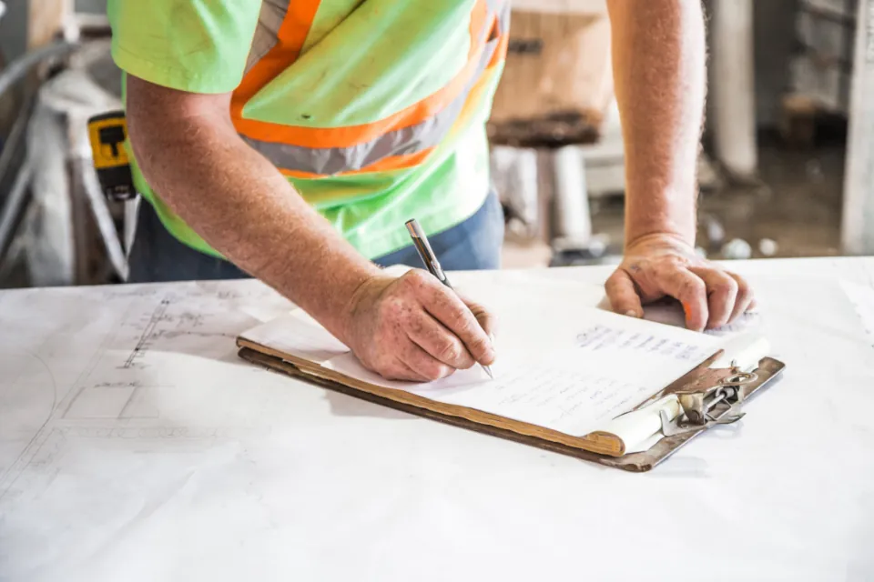 Worker in a safety vest writing on a clipboard over construction plans