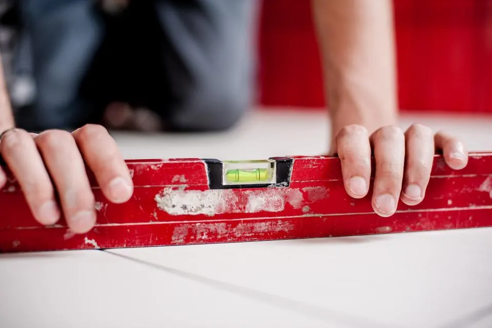 Hands holding a red spirit level against a flat surface