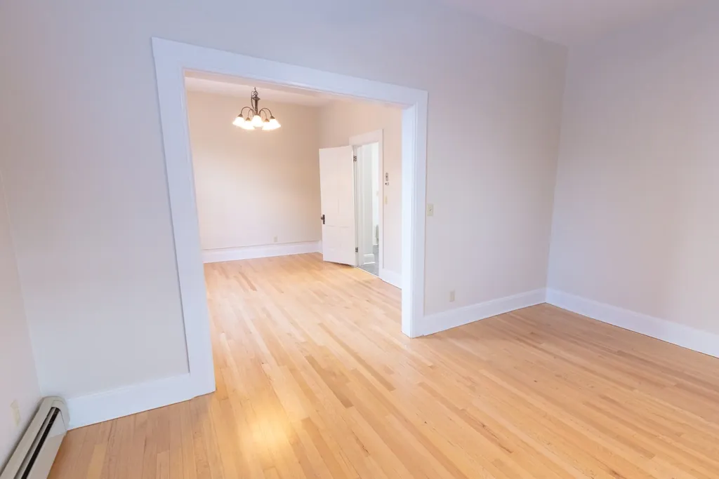 Empty room with light hardwood floors and a doorway to a dining room