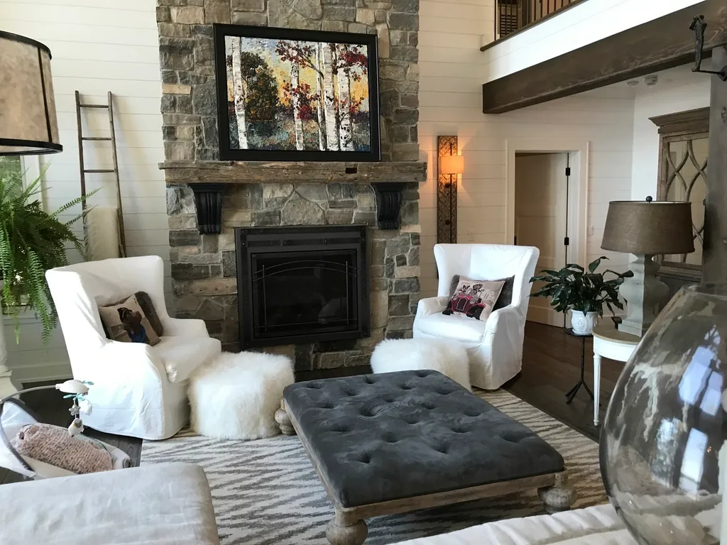 Living room with a stone fireplace, white armchairs and a tufted ottoman