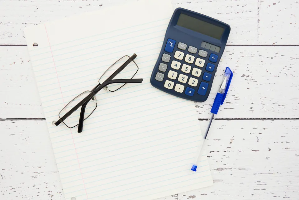 Calculator, eyeglasses and a pen on a lined notepad Calculator, eyeglasses and a pen on a lined notepad