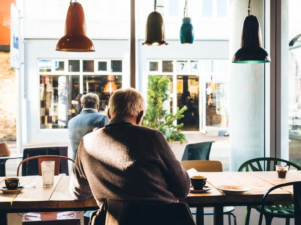 Man seen from behind at a cafe table by a large front window