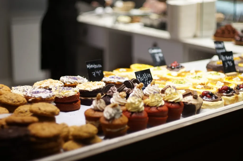 Muffins and pastries with small chalkboard labels in a bakery display case