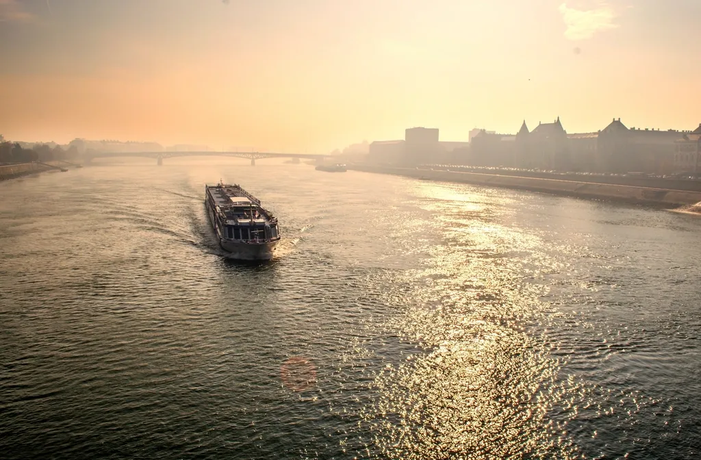 River cruise boat sailing toward a city at sunset