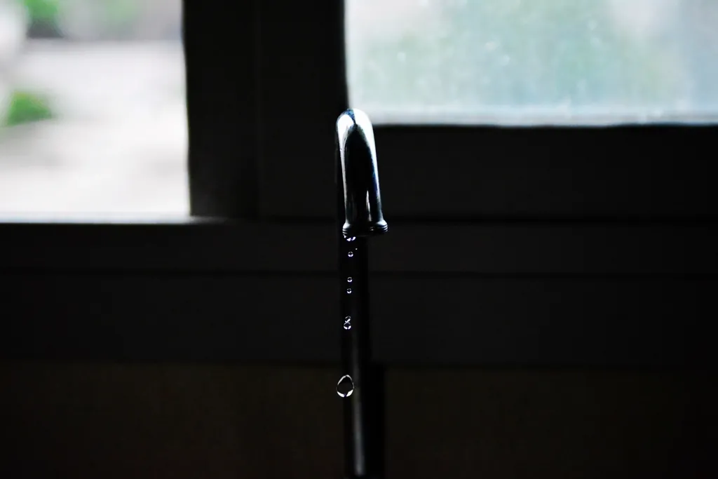 Faucet slowly dripping water near a window Faucet slowly dripping water near a window