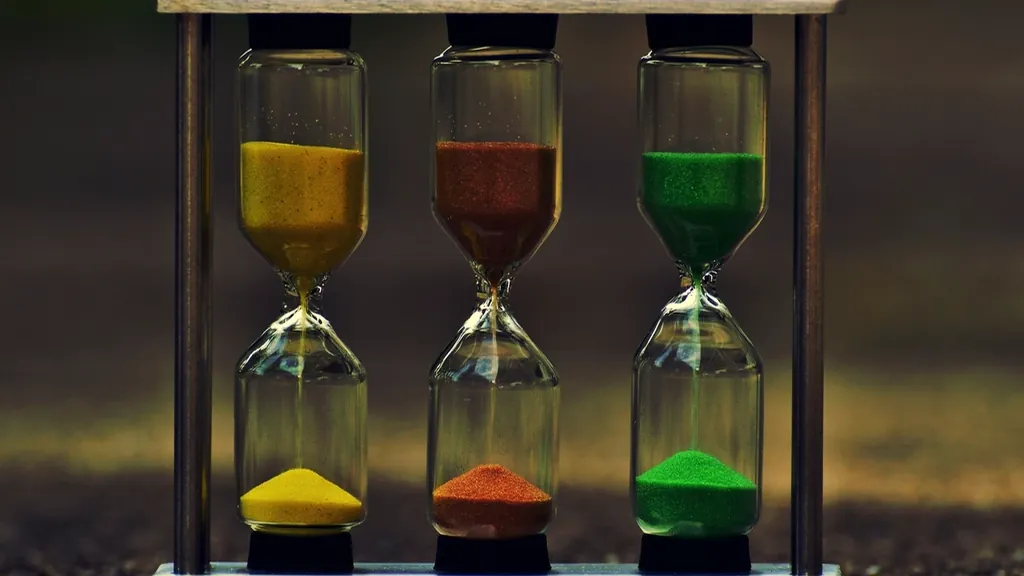 Three hourglasses with colored sand, a symbol of the long wait in private markets for individual investors