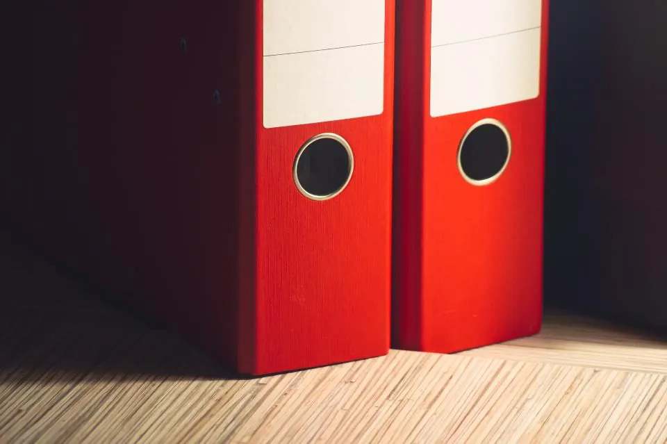 Two red ring binders standing on a wooden floor