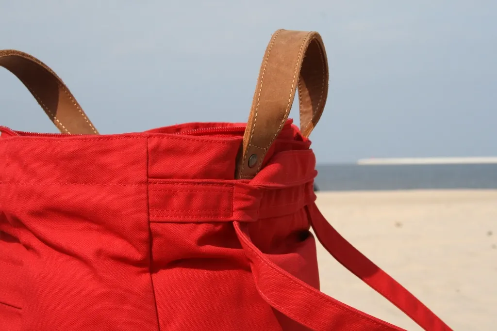 Red canvas tote bag with leather handles on a sandy beach