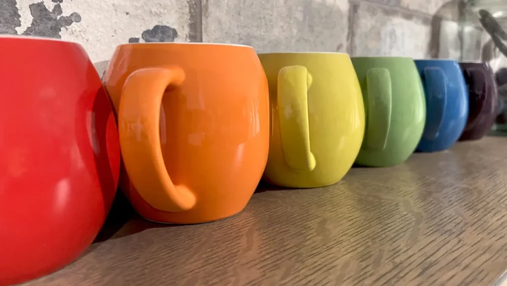 Row of colorful ceramic mugs on a wooden shelf