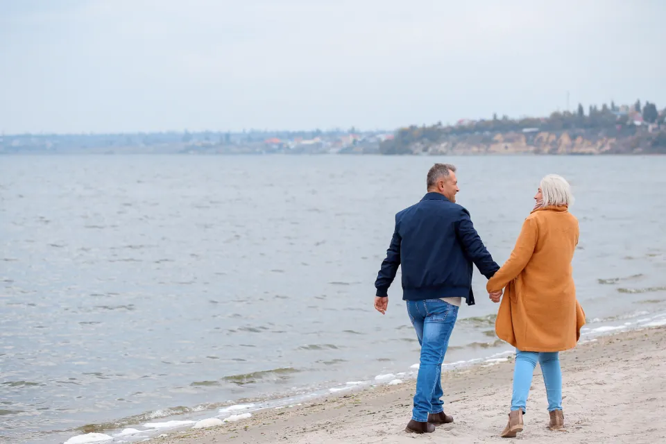 Older couple walking along a sandy beach, seen from behind