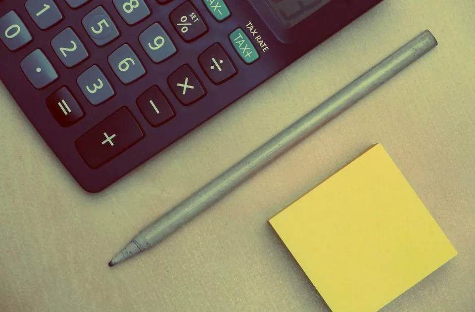 Calculator, pencil and a yellow sticky note on a desk
