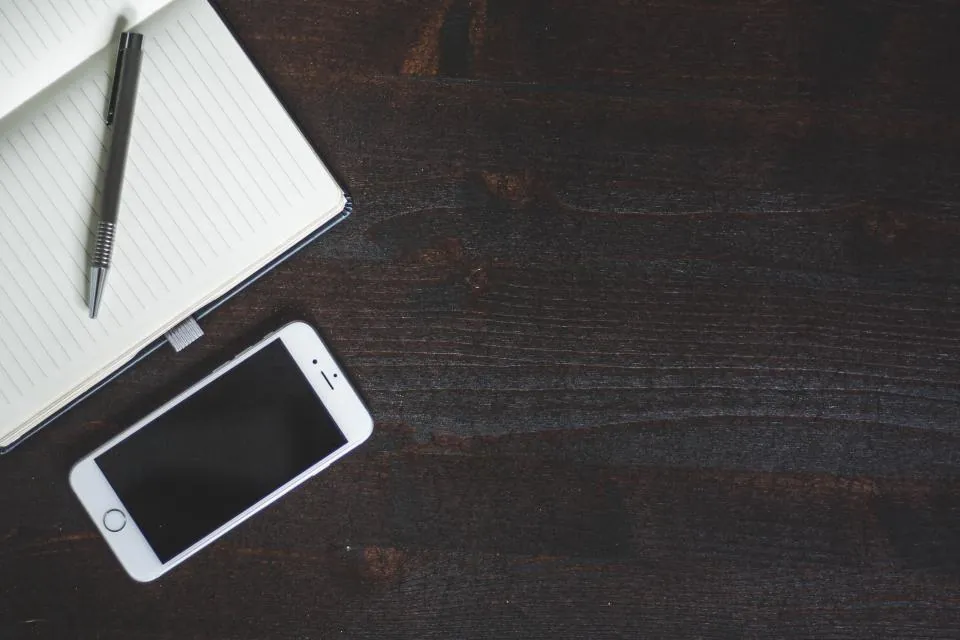 Open notebook with a pen beside a smartphone on a dark wooden desk