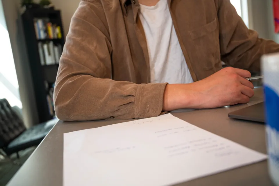 Person at a desk with a pen and printed papers in a home office